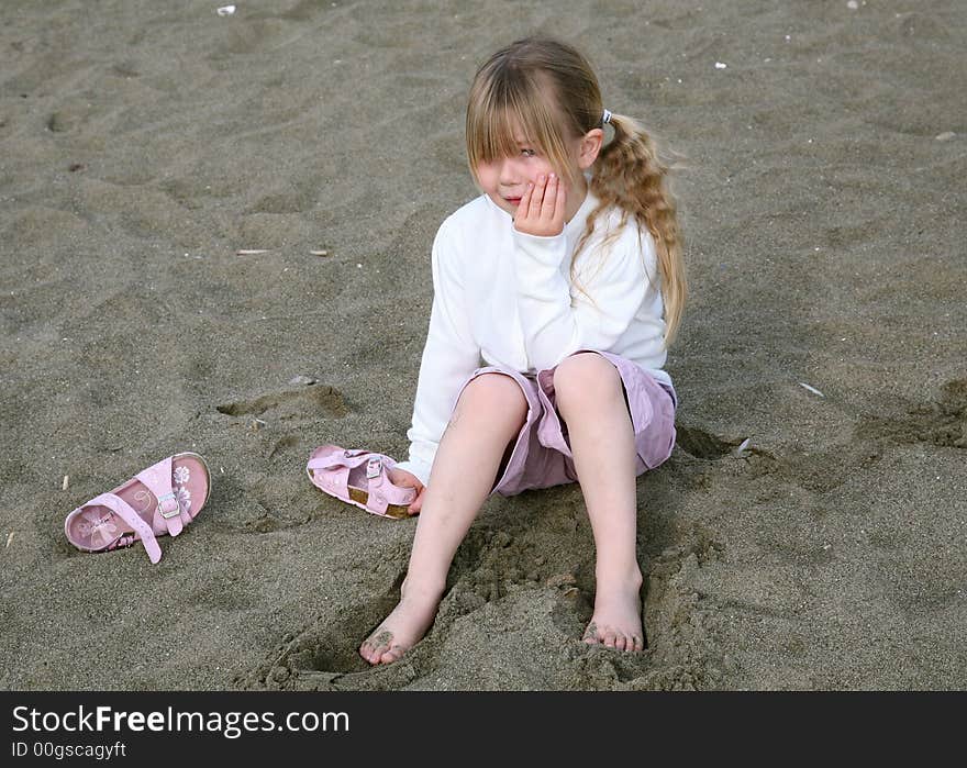 A young girl having a tantrum sat on a beach. A young girl having a tantrum sat on a beach