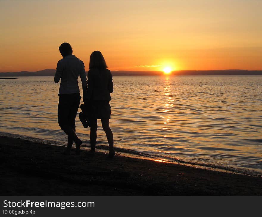 He and she walking near the sea at sunset