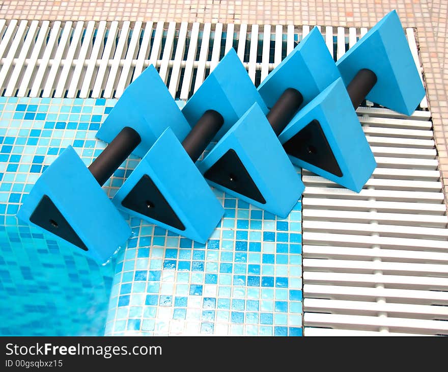 Four blue aqua dumbbells lie on the coast swimming-pool