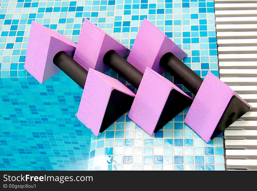 Three pink aqua dumbbells lie on the coast swimming-pool