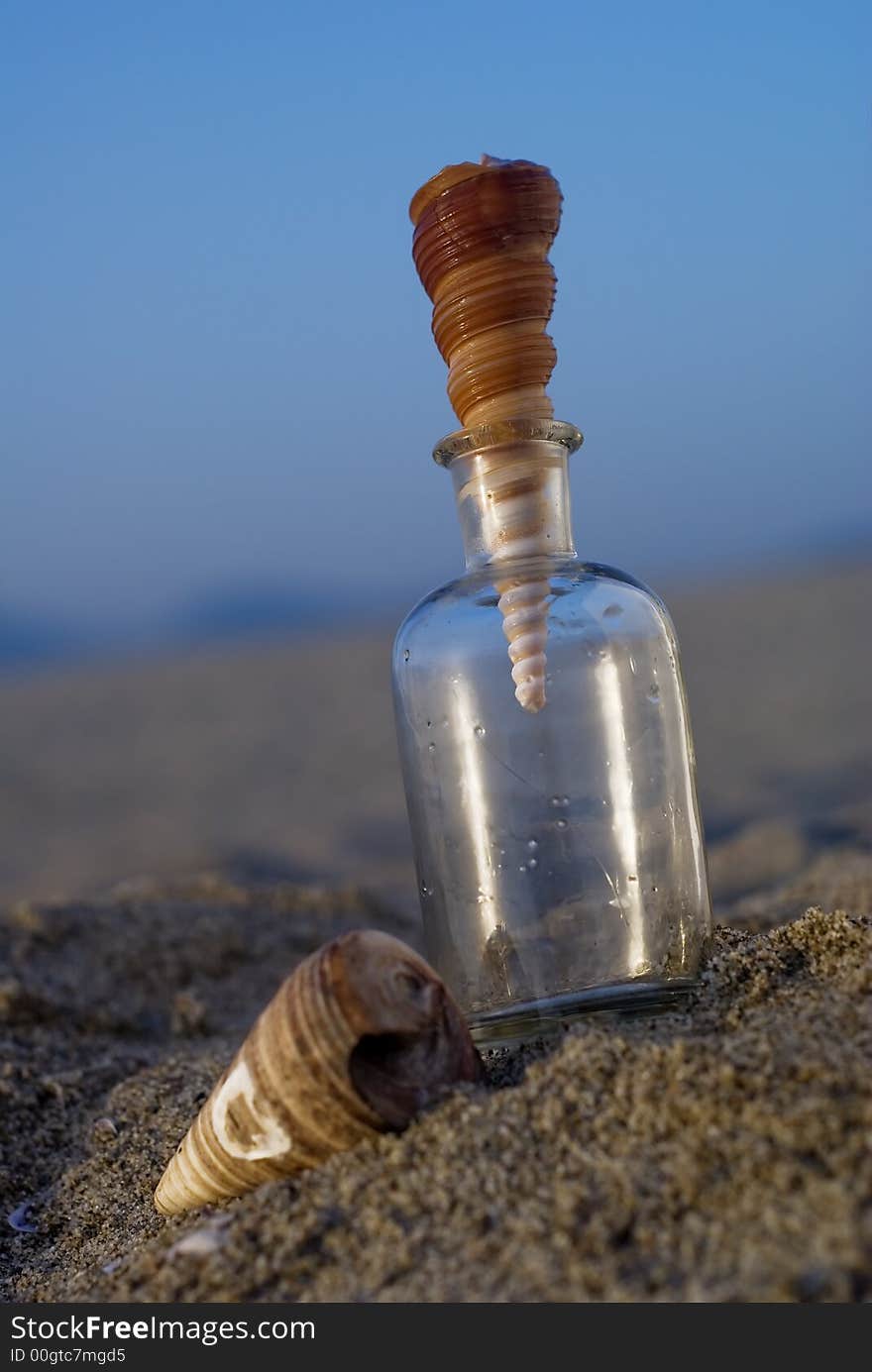 Summer composition with a glass bottle and beautiful shell at sunset. Summer composition with a glass bottle and beautiful shell at sunset