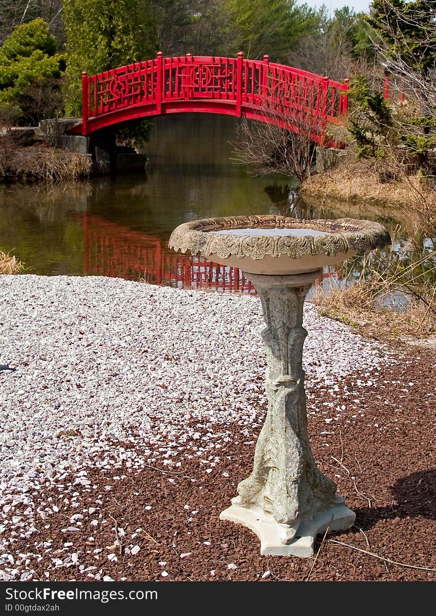 An old stone birdbath with a colorful bridge in the background. An old stone birdbath with a colorful bridge in the background.