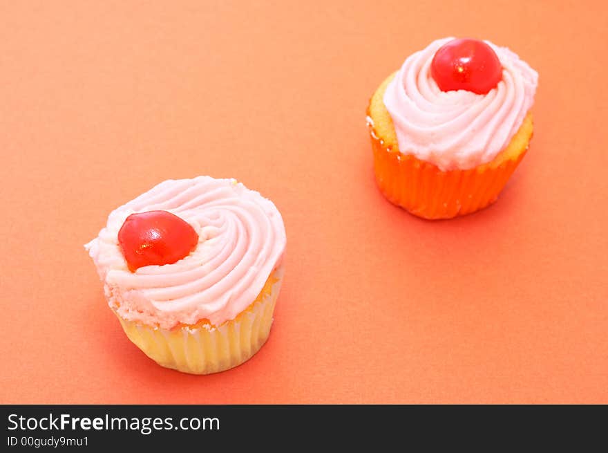 Two colorful vanilla cupcakes on orange paper background. Focus on front cupcake