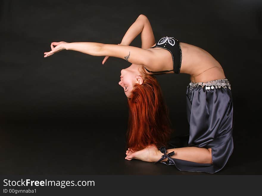 Red-headed girl in bellydance costume standing on her knees and bending backwards. Red-headed girl in bellydance costume standing on her knees and bending backwards