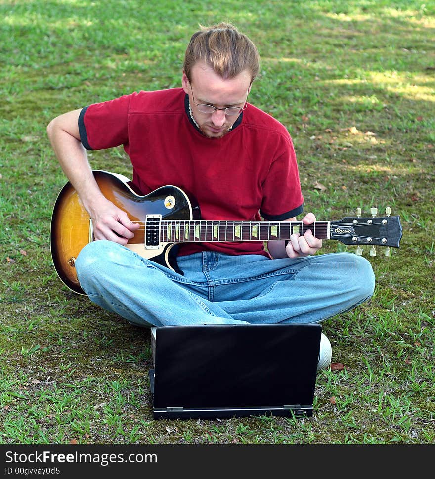 A guitarist plays in the out of doors with the assistance of his laptop. A guitarist plays in the out of doors with the assistance of his laptop.