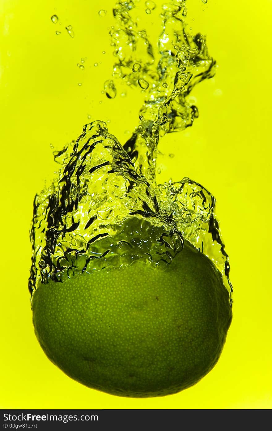 A lime plunging into water with a yellow background. A lime plunging into water with a yellow background