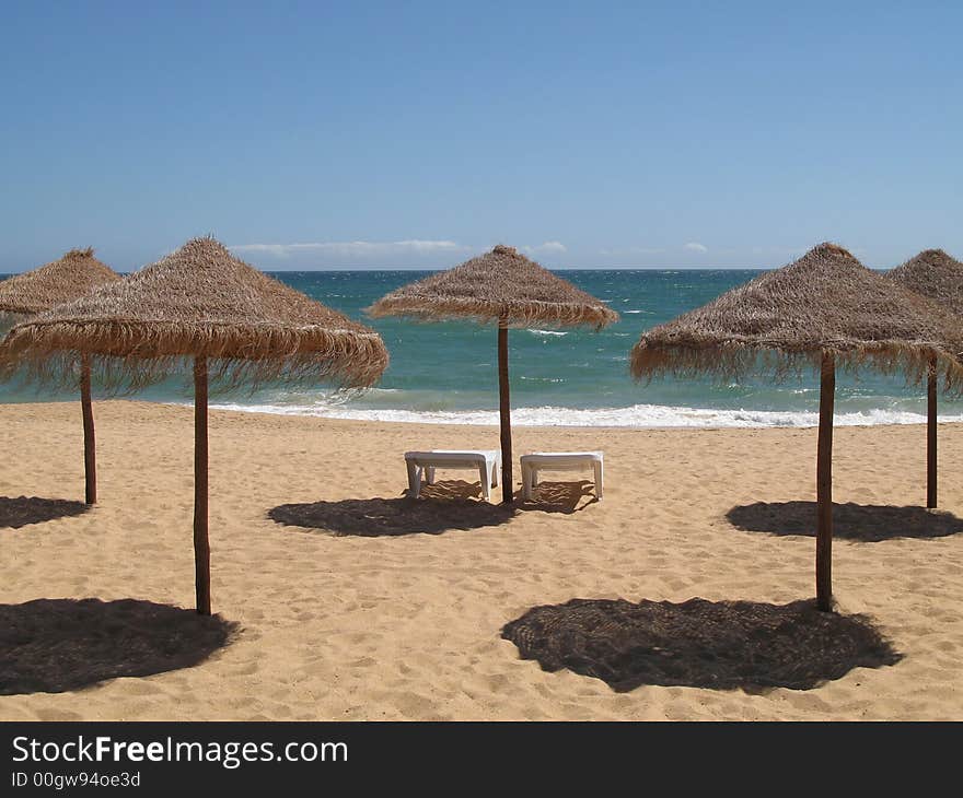 Two sun lounges and palm umbrellas on a beach. Two sun lounges and palm umbrellas on a beach