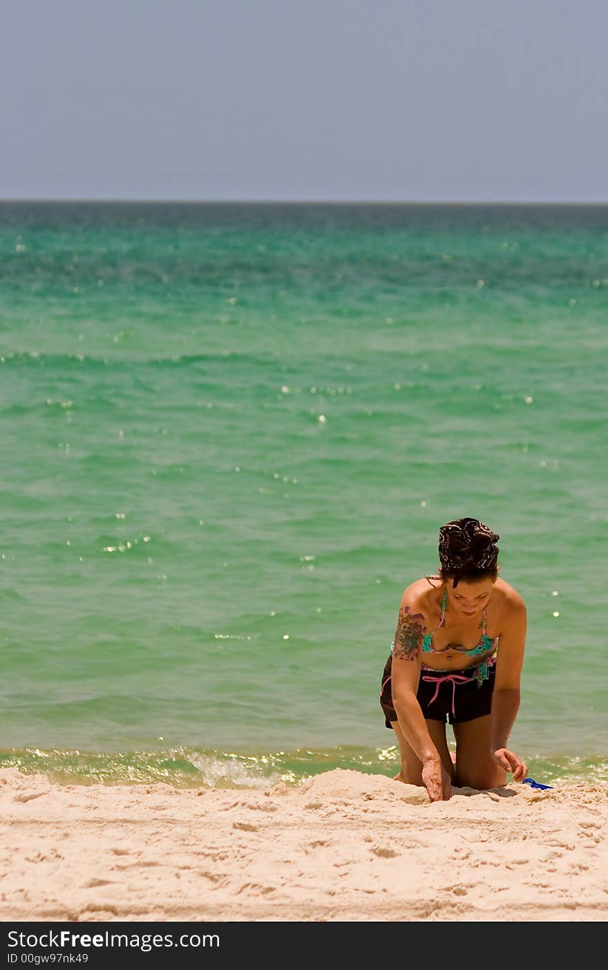 A pretty young woman with a tattoo in a bikini works on a sand sculpture at the beach. A pretty young woman with a tattoo in a bikini works on a sand sculpture at the beach.