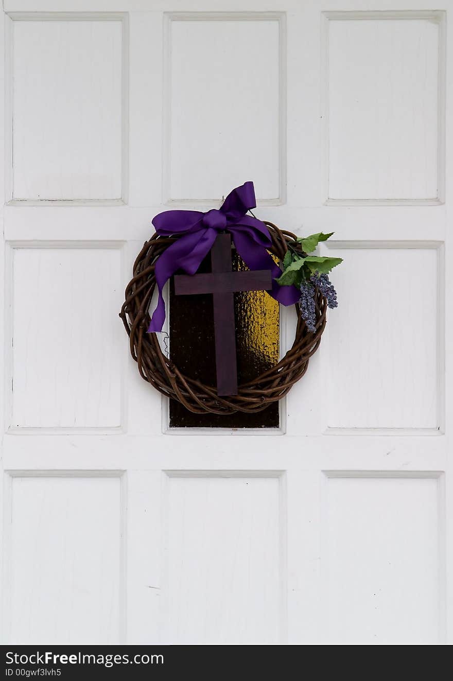 Wood cross hanging on a white door with a purple ribbon and a wreath. Wood cross hanging on a white door with a purple ribbon and a wreath