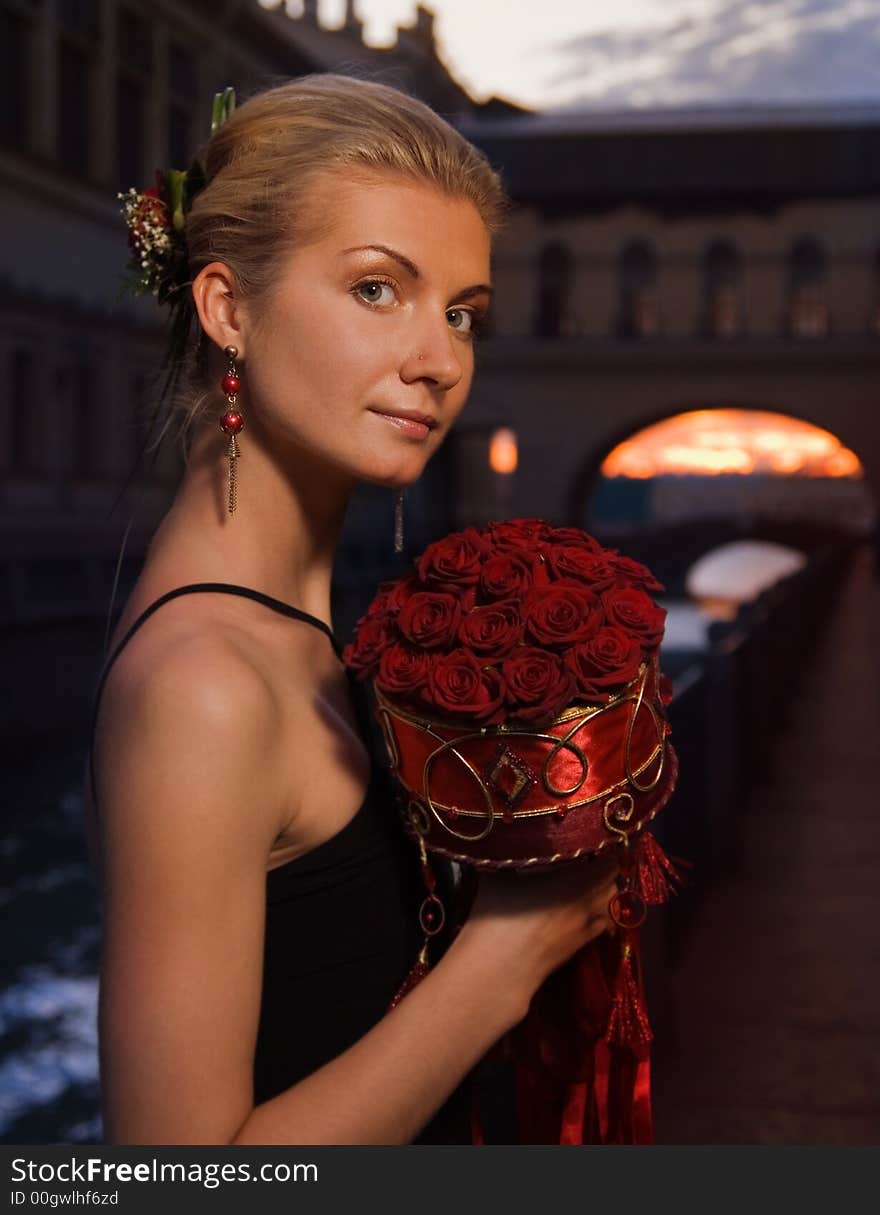 Beautiful blond girl with a boquet of roses at sunset time near the river