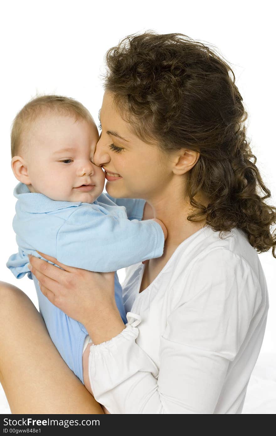 Young happy mother hugging baby. Woman is sitting in bed, baby is sitting on her. White background. Young happy mother hugging baby. Woman is sitting in bed, baby is sitting on her. White background