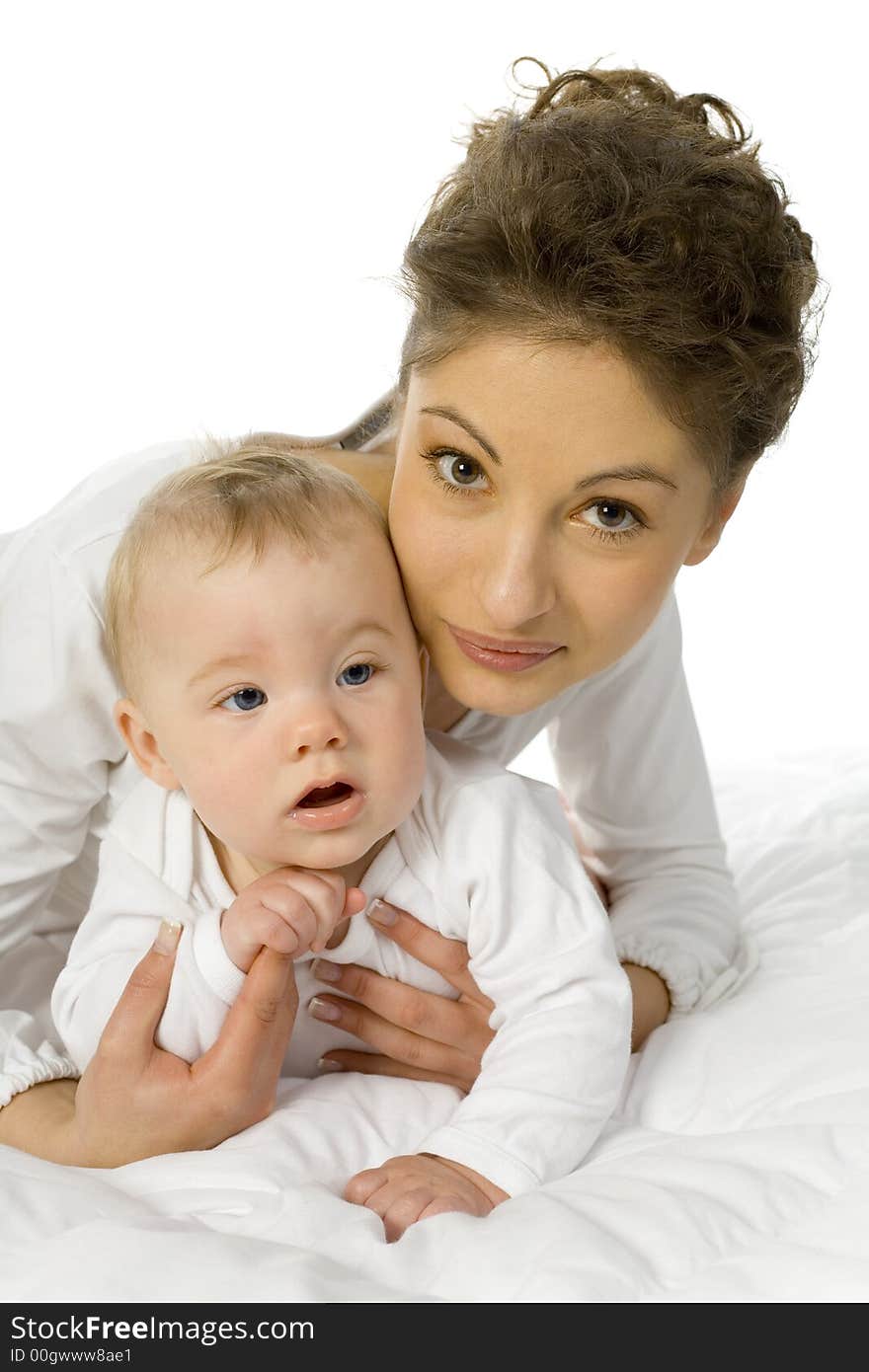 Young happy mother holding baby. Woman is lying in bed, holding baby. White background, looking at camera. Young happy mother holding baby. Woman is lying in bed, holding baby. White background, looking at camera