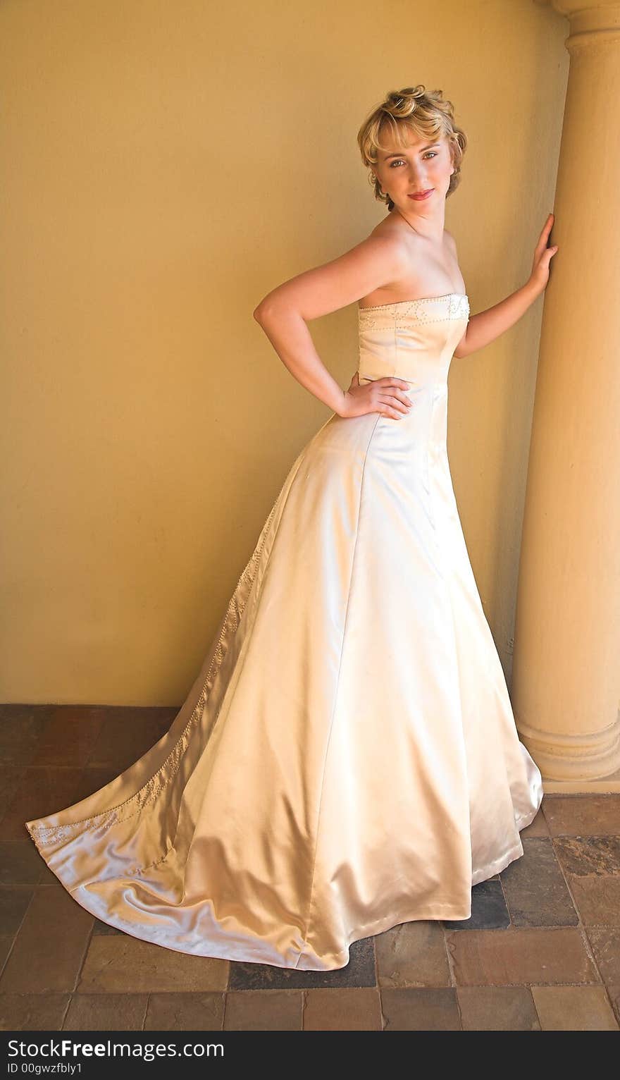 Beautiful blond bride with short hair in beige pearl dress leaning against a pillar. Beautiful blond bride with short hair in beige pearl dress leaning against a pillar