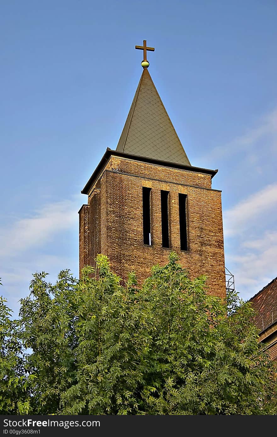 Old red brick church tower with iron cross.