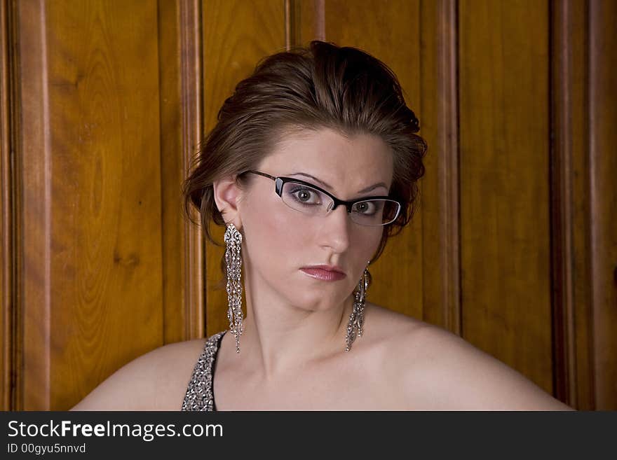 Beautiful young brunette in glasses and a dress looking intently at the camera. Brown vintage door in background. Beautiful young brunette in glasses and a dress looking intently at the camera. Brown vintage door in background.