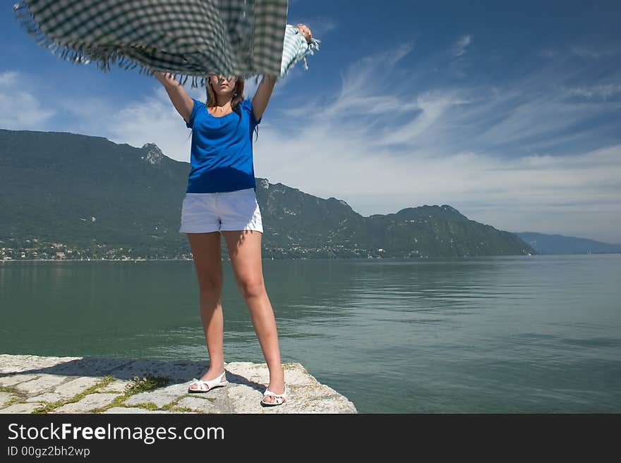 Woman extending a tablecloth for a picnic at the edge of a lake