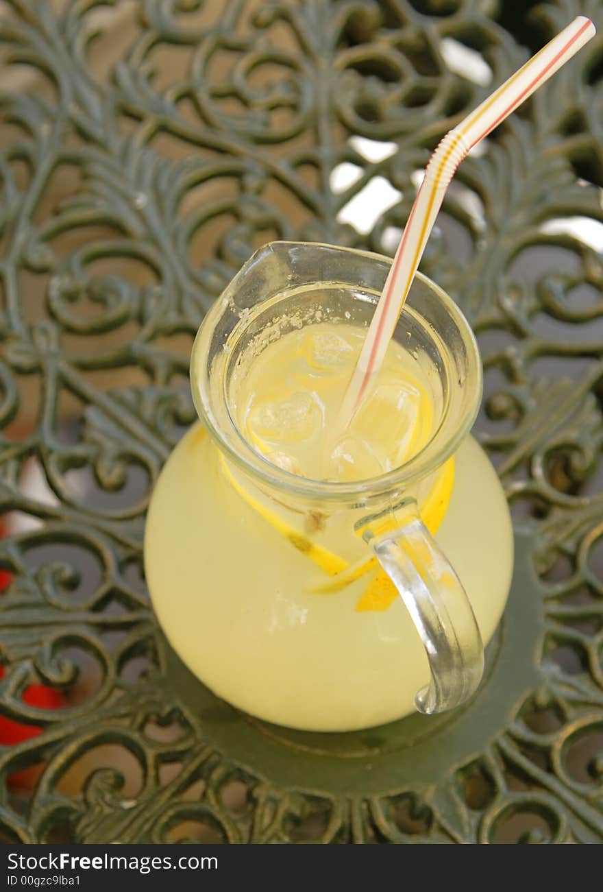 Upper view of a big cup with lemonade with a straw.The background represent an elegant coffee bar table.