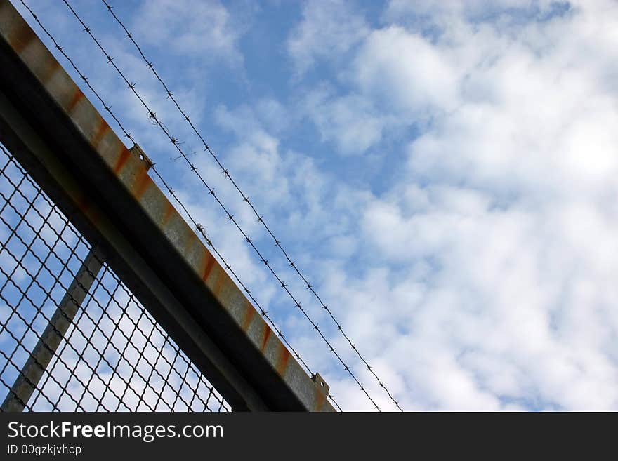 Barbed wire on a rusty fence in front of blue cloudy sky. Barbed wire on a rusty fence in front of blue cloudy sky