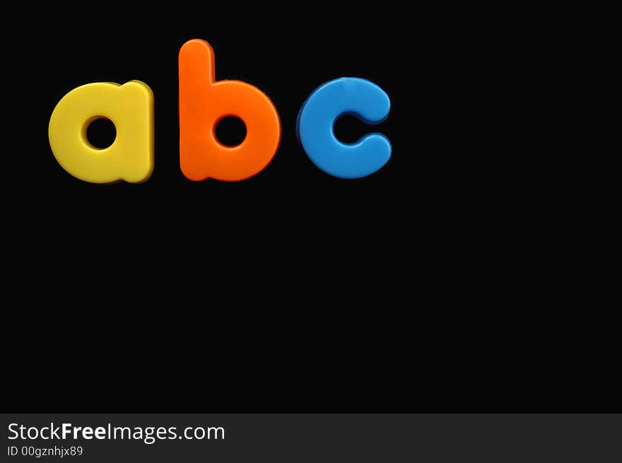 The letters a, b and c from a child's toy alphabet set, placed on a black background. Space for text elsewhere in the image. The letters a, b and c from a child's toy alphabet set, placed on a black background. Space for text elsewhere in the image.