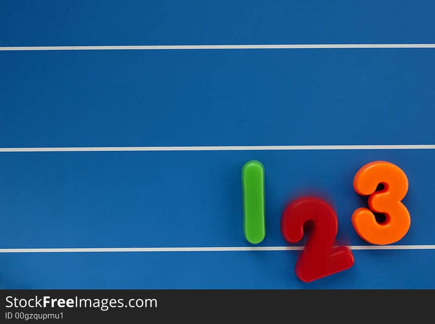 The numbers 1, 2 and 3 from a child's toy learning set, on a blue, lined background. The number 2 dropping out of the line, with motion blur. The numbers 1, 2 and 3 from a child's toy learning set, on a blue, lined background. The number 2 dropping out of the line, with motion blur.