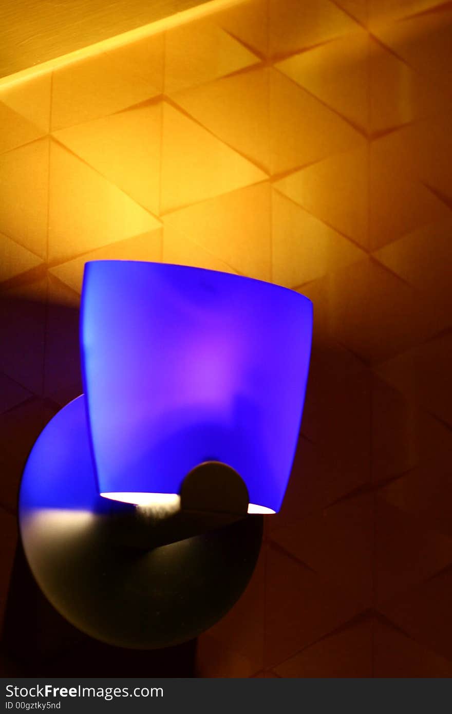 A modern blue light fixture against a gold wall. A modern blue light fixture against a gold wall