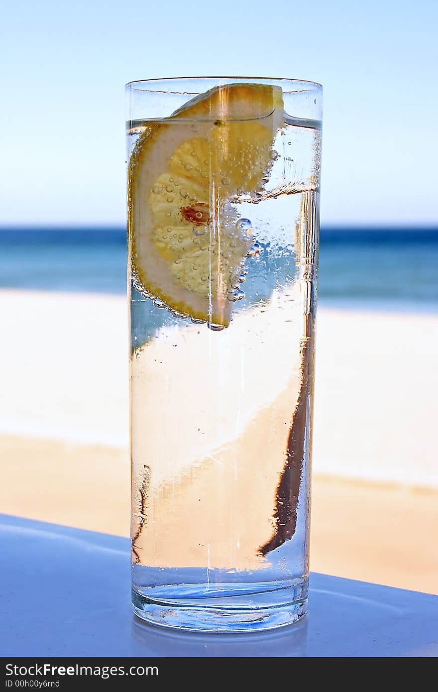 Fresh glass of bubble water with a slice of lemon at the beach