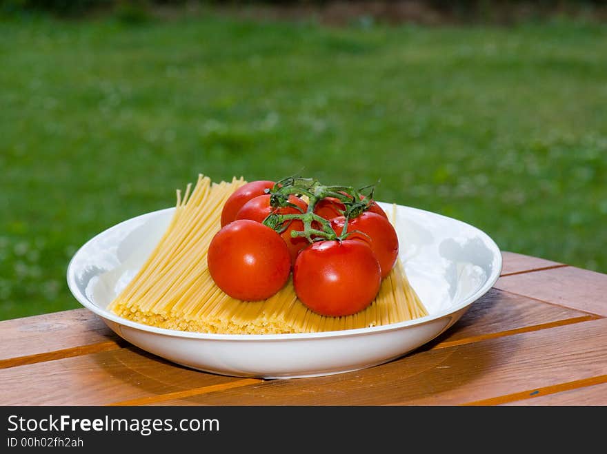 plate with spaghetti and tomato on table in garden. plate with spaghetti and tomato on table in garden