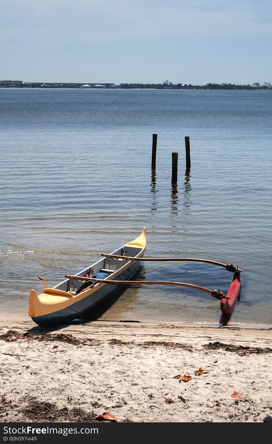 Colorful outrigger canoe beached at the shore.
Vertical orientation.  Blue sky, calm waters.