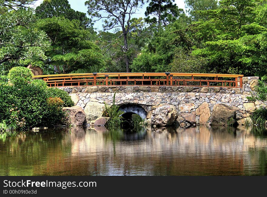 Stone bridge over lake in a pristine garden environment. Reflection of bridge in water.