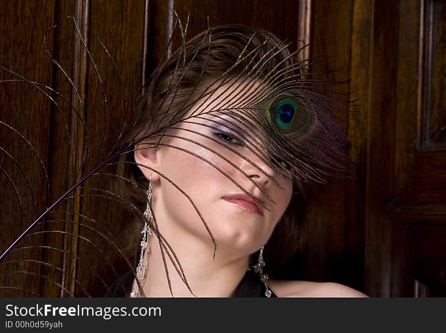 Beautiful young brunette woman with a feather partially covering her face. Dark wood background. Beautiful young brunette woman with a feather partially covering her face. Dark wood background.