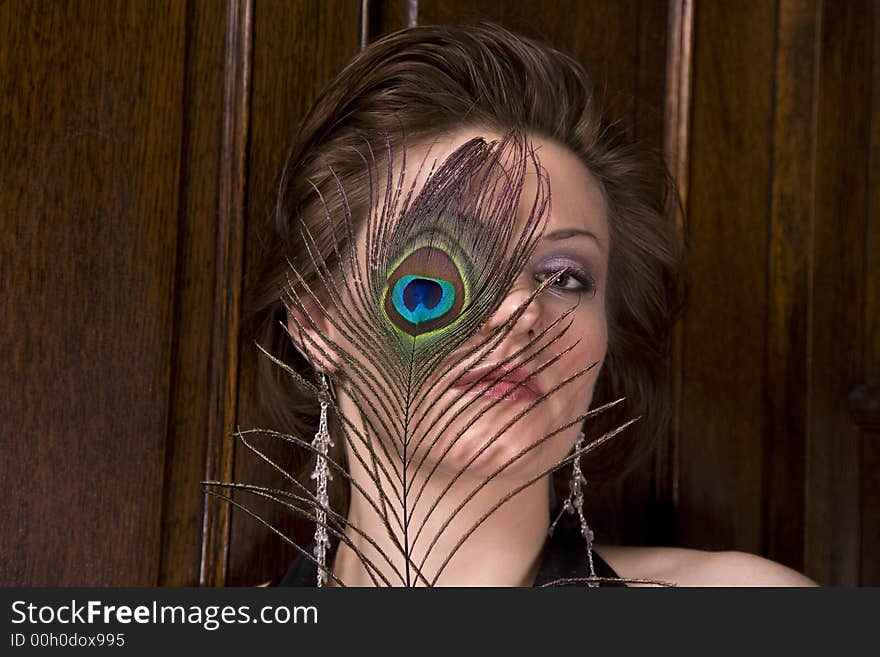 Beautiful young brunette woman with a feather partially covering her face. Dark wood background. Beautiful young brunette woman with a feather partially covering her face. Dark wood background.