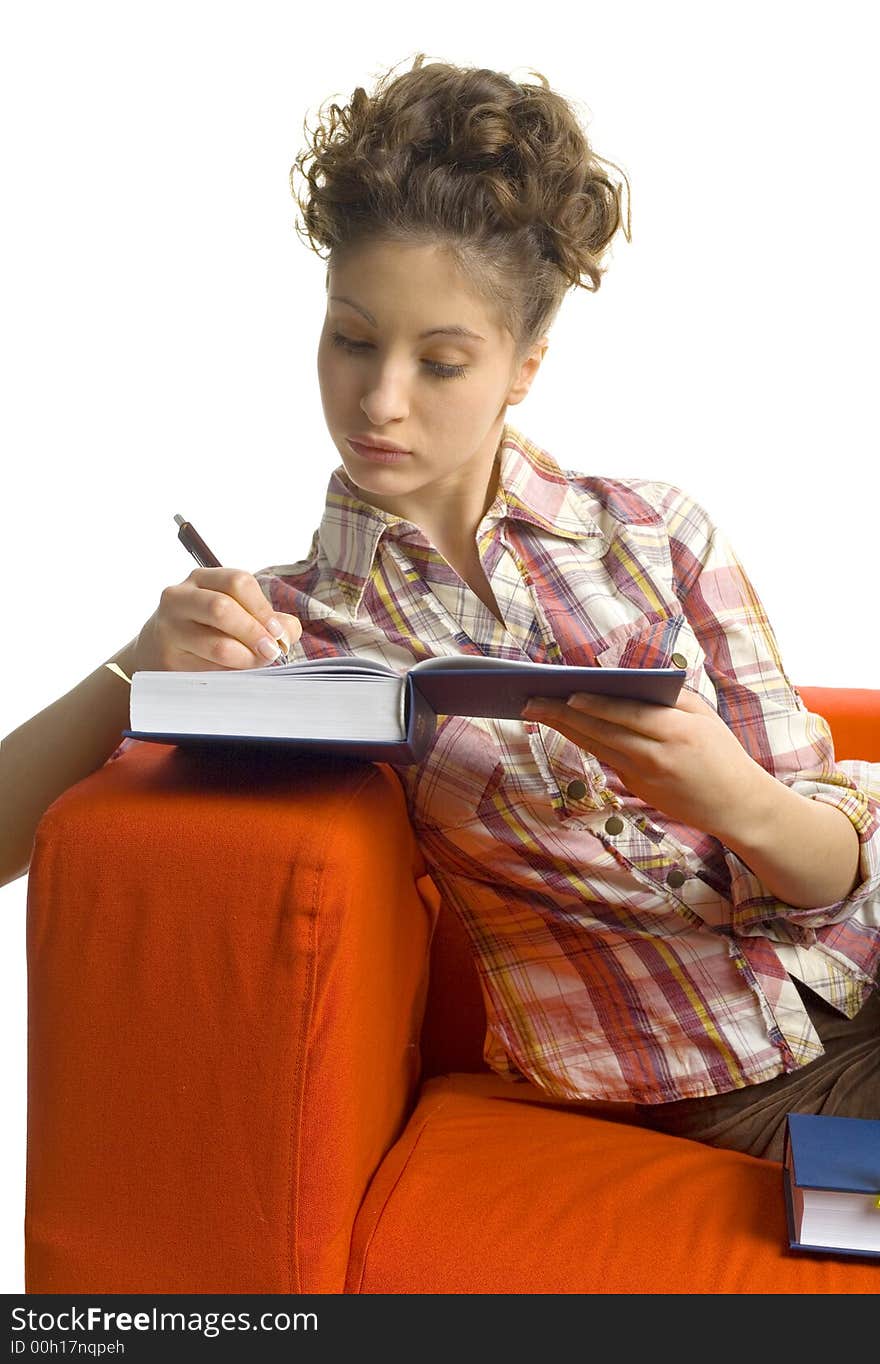 Young, beautiful woman sitting on orange couch. Writing on book. White background. Young, beautiful woman sitting on orange couch. Writing on book. White background