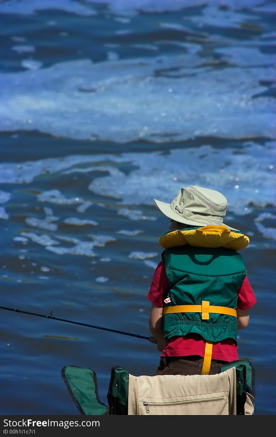 Little boy with a teal green armless life-jacket and a tilley style hat on fishing with lots of copyspace above. Little boy with a teal green armless life-jacket and a tilley style hat on fishing with lots of copyspace above.