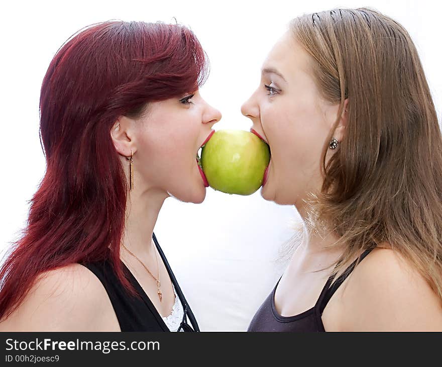 Two girls bite a green apple. Two girls bite a green apple