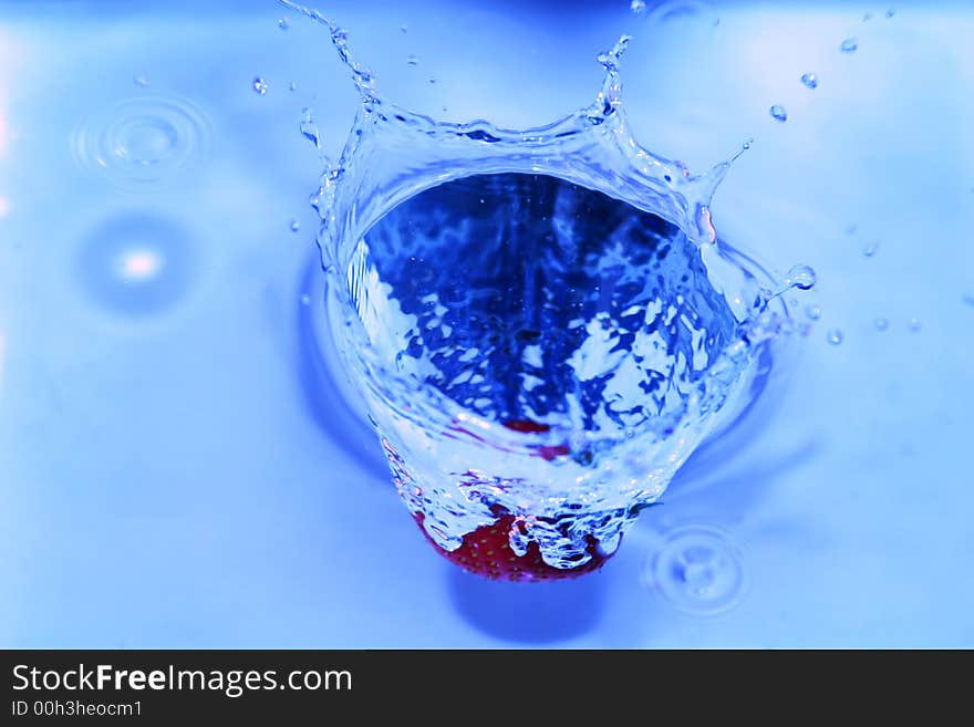 Strawberry dropped into water making a splash, macro shot. Strawberry dropped into water making a splash, macro shot