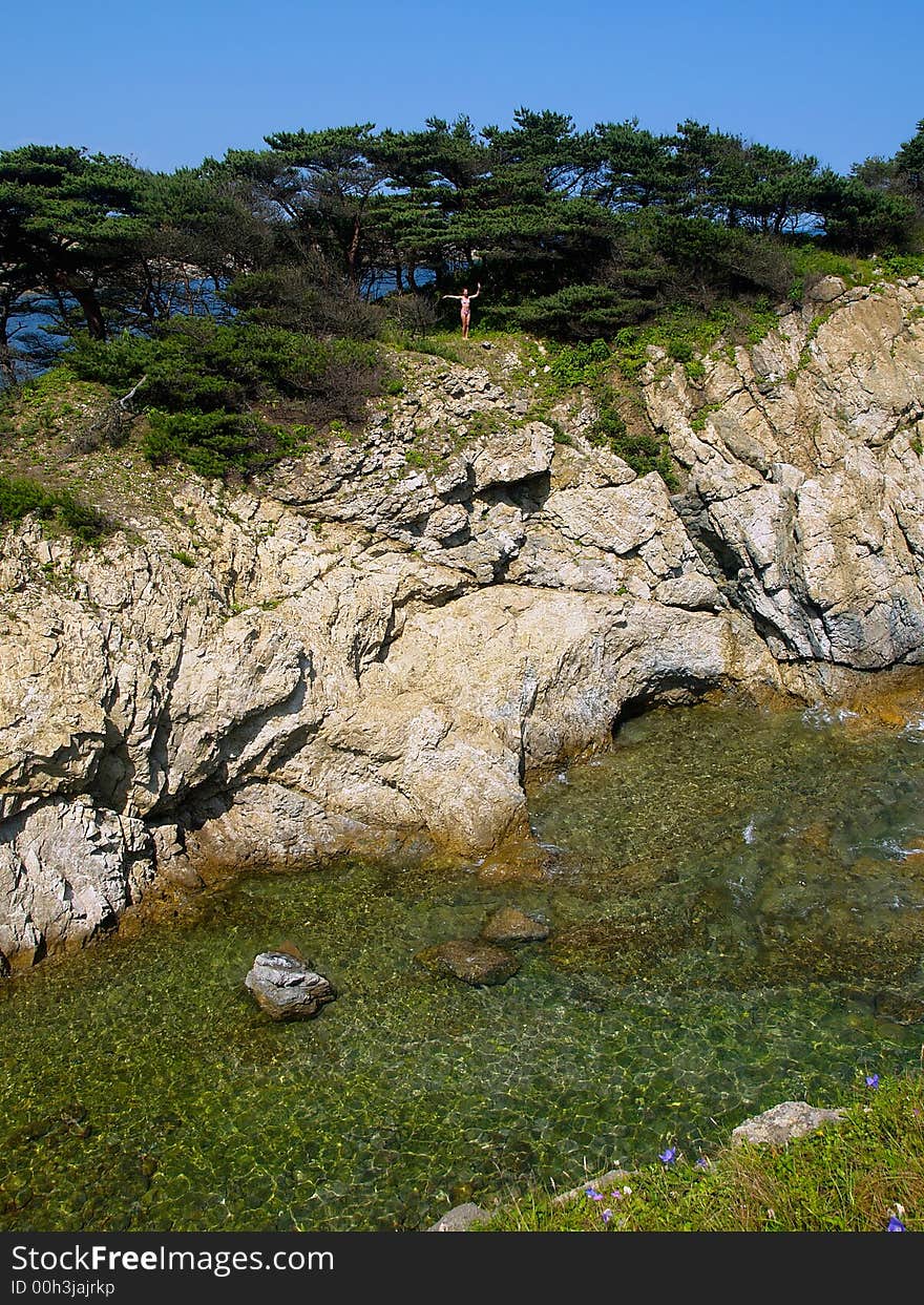 sea landscape showing young girl standing on the seaside rock with pines