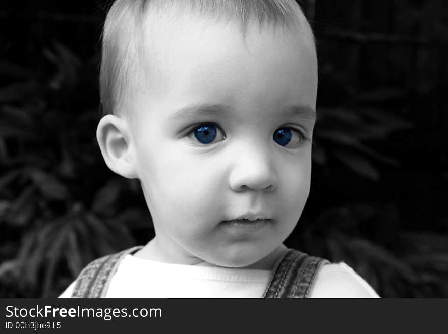 This is a close-up of a young child with vibrant blue eyes in which the eyes are in color and the rest of the photo is in black and white.