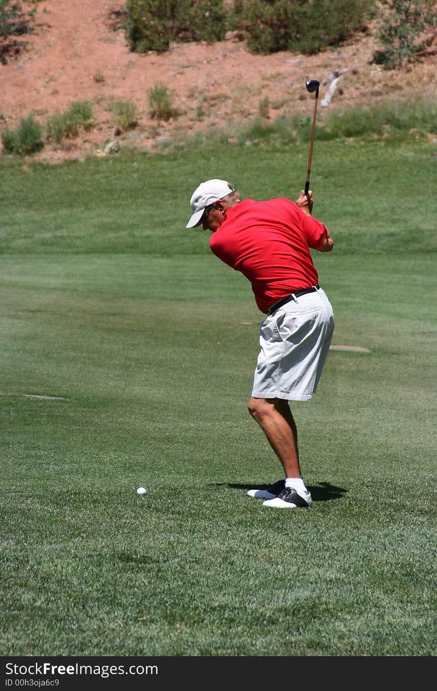 Male about to hit ball from the fairway (towards camera), focus on golfer. Male about to hit ball from the fairway (towards camera), focus on golfer