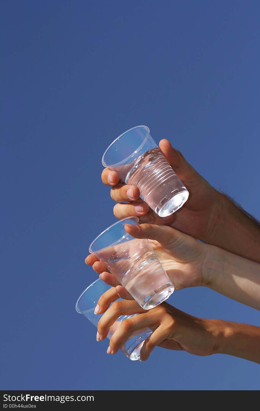 Glasses with transparent beverage in hands against a blue sky. Glasses with transparent beverage in hands against a blue sky