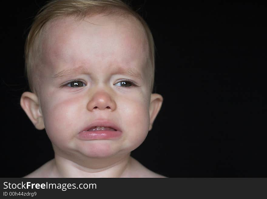 Image of crying toddler sitting in front of a black background