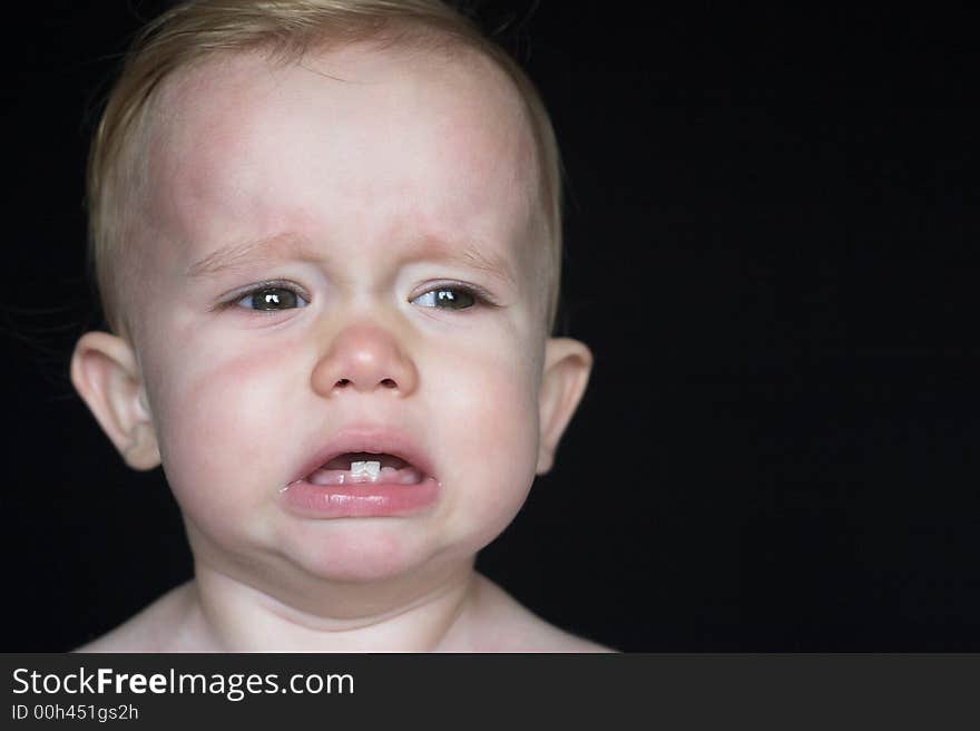 Image of crying toddler sitting in front of a black background