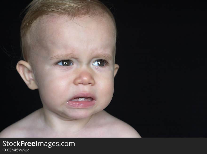 Image of crying toddler sitting in front of a black background