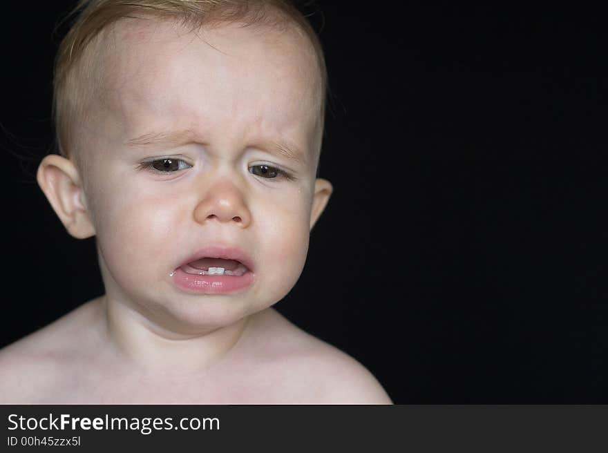 Image of crying toddler sitting in front of a black background