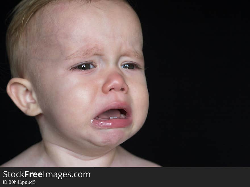 Image of crying toddler sitting in front of a black background