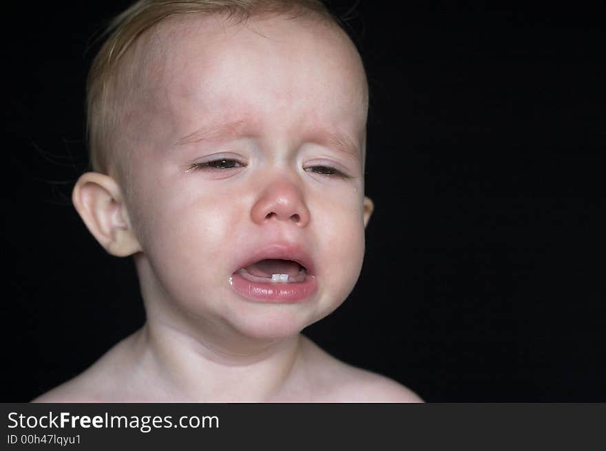 Image of crying toddler sitting in front of a black background