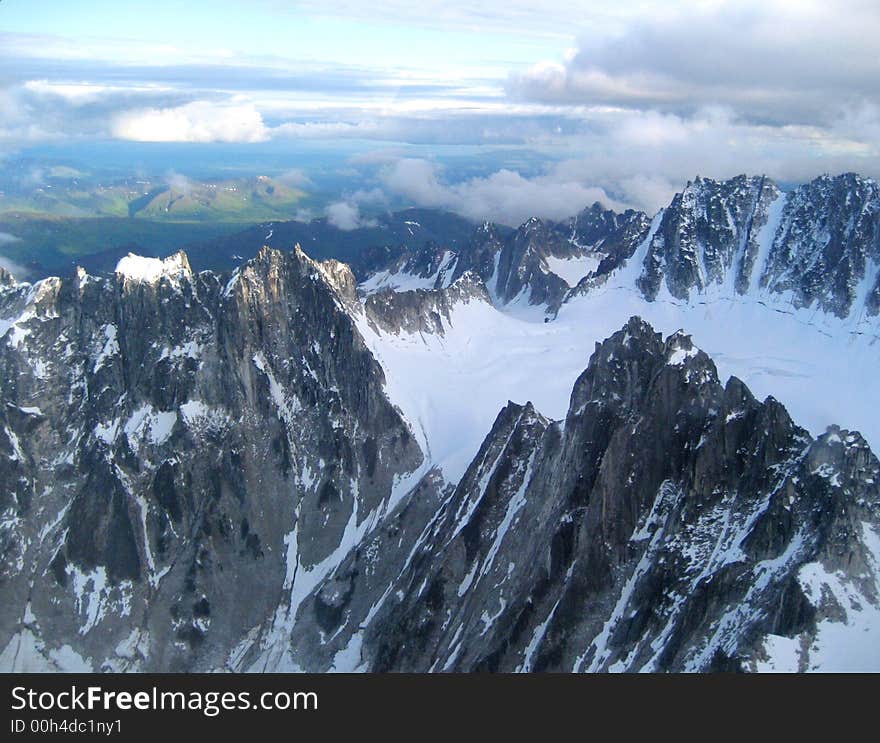 Flying over Alaska, snowy mountains of rock, green ranges in the background. Flying over Alaska, snowy mountains of rock, green ranges in the background