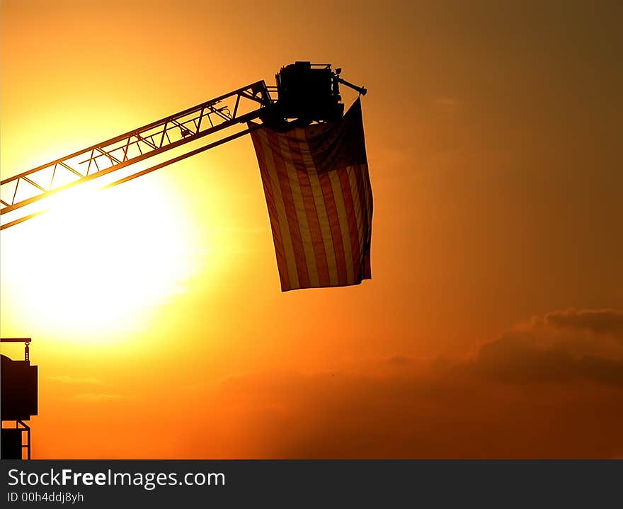 An American flag hanging in the sunset on the top of a fire truck ladder. An American flag hanging in the sunset on the top of a fire truck ladder.