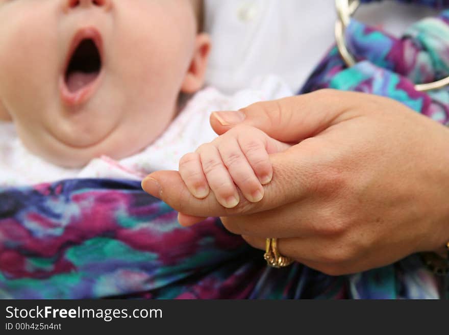 The hands of a mother and child with a baby yawning in the background. The hands of a mother and child with a baby yawning in the background