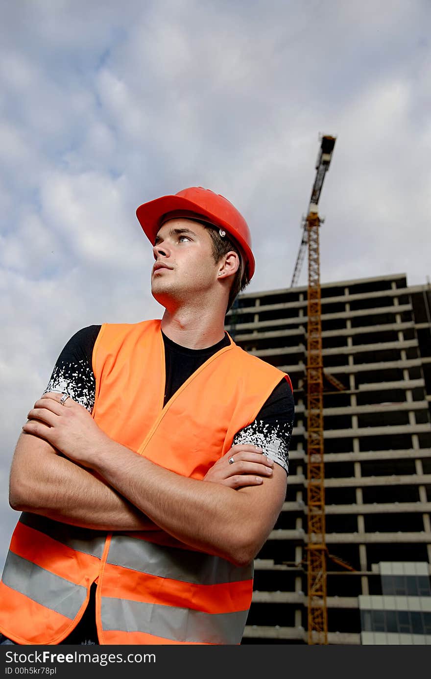 Construction supervisor in safety helmet and reflex vest in front of construction site.