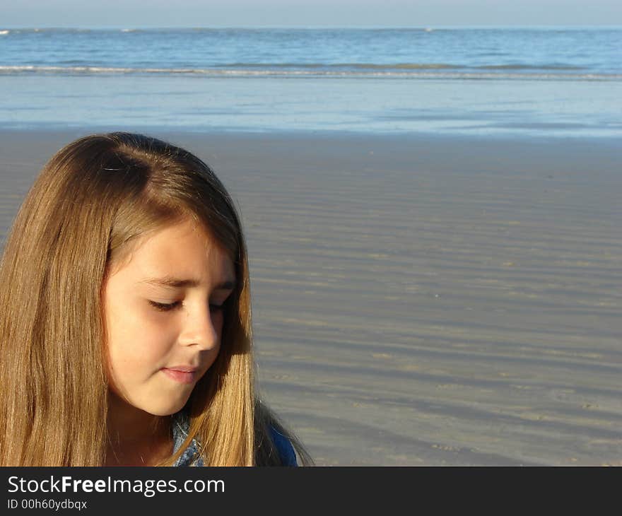 Young girl standing on the beach, looking at the sand. Young girl standing on the beach, looking at the sand